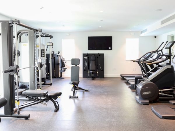 The image shows a modern gym with fitness equipment, including treadmills, weight machines, and benches, set in a well-lit room.