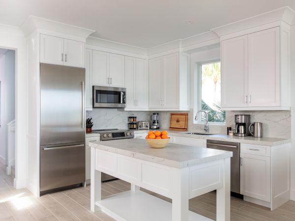 A modern kitchen with white cabinets, stainless steel appliances, and a central island with a bowl of oranges on top of it.