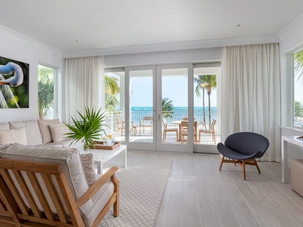 A bright and modern living room with wooden furniture, a TV, and a view of the ocean through large windows and sliding doors.