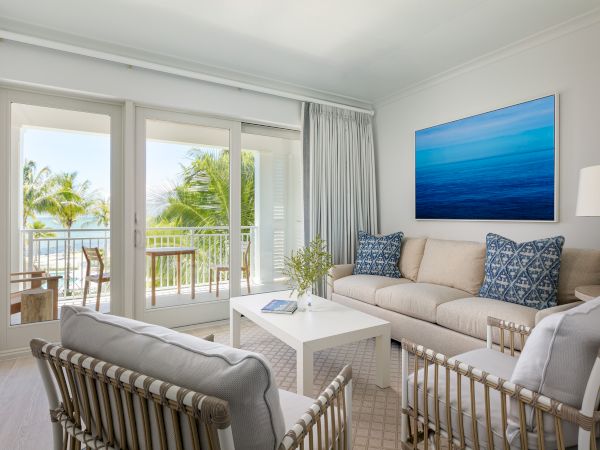 A bright, modern living room with a view of a balcony. Furnished with a beige sofa, decorative pillows, armchairs, a coffee table, and wall art.
