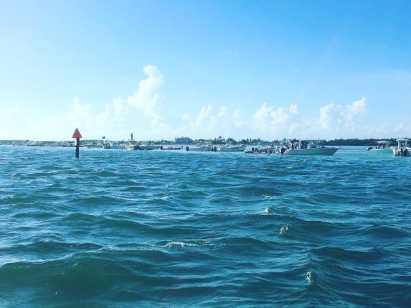 The image shows a vast expanse of water under a clear blue sky, with distant boats and a navigation marker visible in the background.