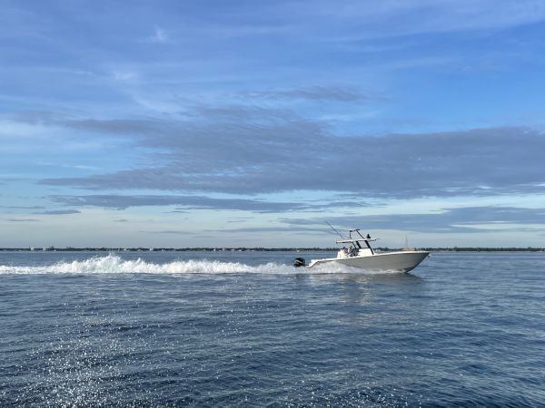A motorboat speeds across a calm, blue ocean under a clear sky, leaving a white wake behind it.