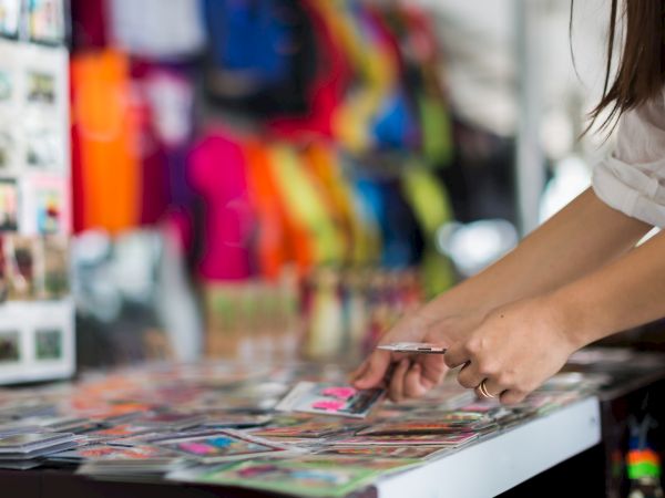 A person is browsing through a collection of colorful photographs or postcards on a table, with vibrant clothing in the background.