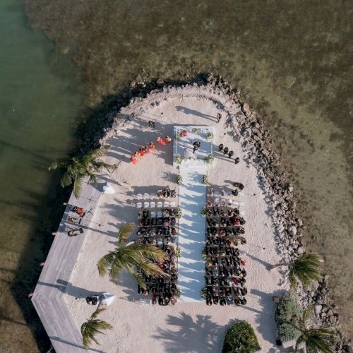 Aerial view of a crowded beach/seafood venue with people on a white terrace beside clear ocean water.