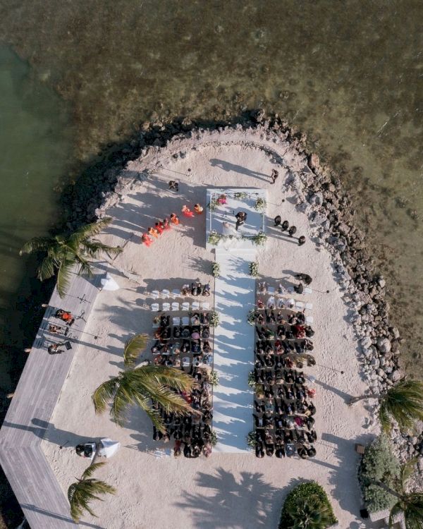 Aerial view of a crowded beach/seafood venue with people on a white terrace beside clear ocean water.