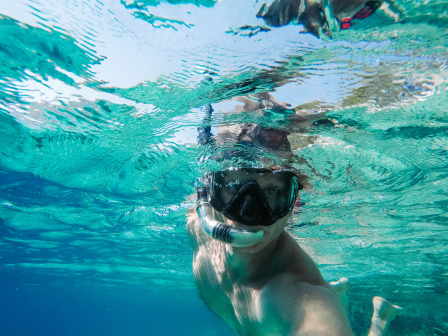 A person is snorkeling underwater, wearing a mask and snorkel, while taking a selfie in clear, blue water.