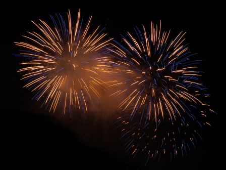 The image shows two bright fireworks bursting in the night sky with a mix of orange and blue colors.