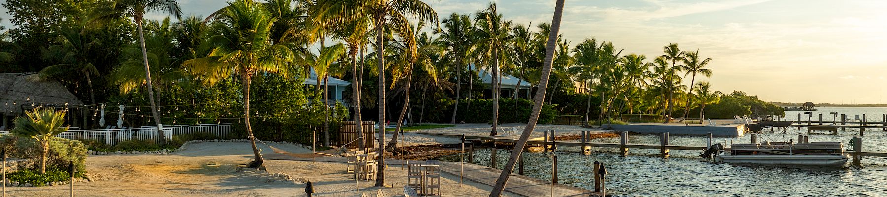 Palm-fringed tropical beach with lounge chairs, a rocky jetty, and calm blue water at sunset; a tranquil island paradise.