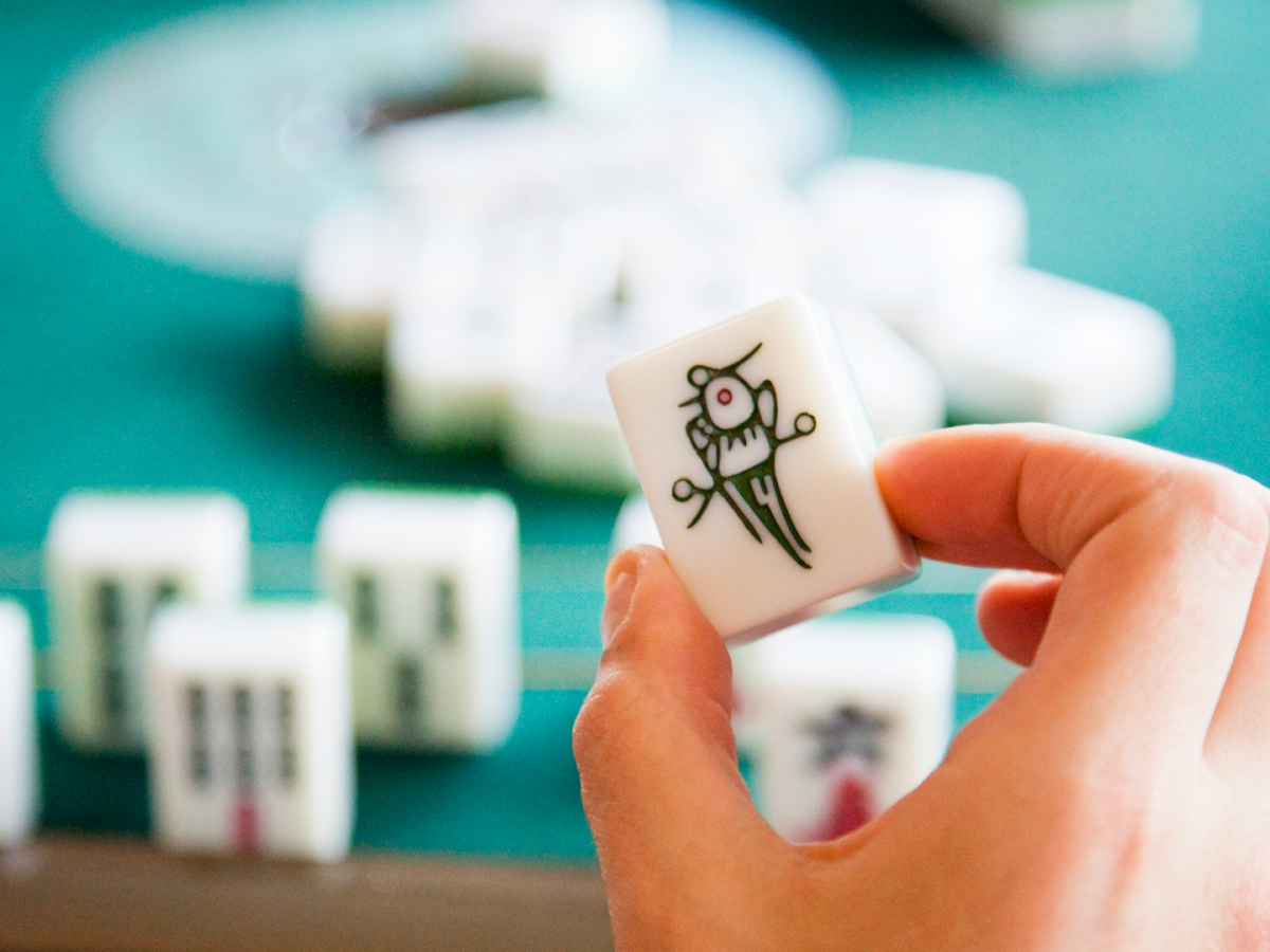 A hand holds a small white card with a cute doodle (bird/flower), in front of a blurred teal building facade.