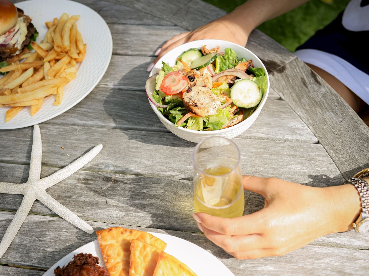 Outdoor lunch with salad and fries as friends clink drinks on a patio table.