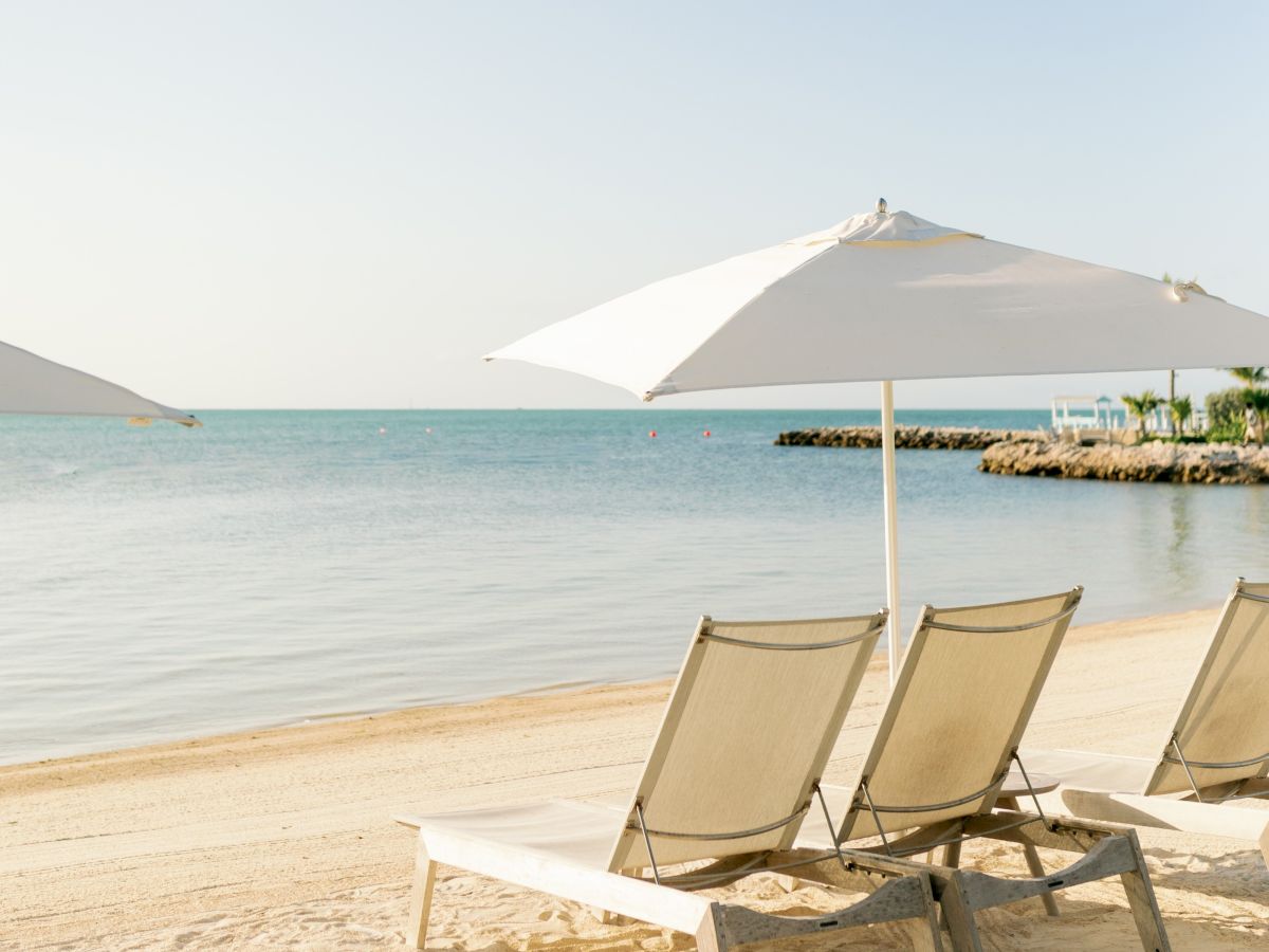 A sunny beach scene with white umbrellas, lounge chairs, and calm ocean waves under a clear sky.